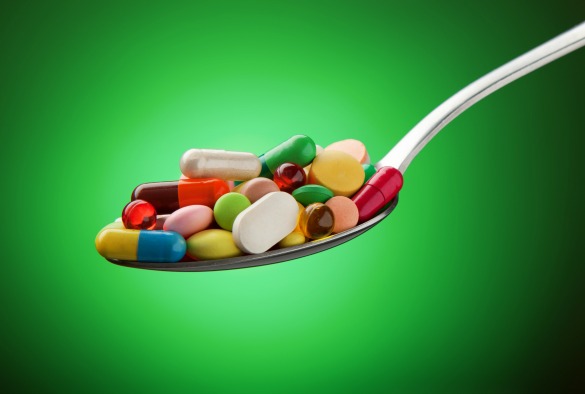 Various pills, capsules and tablets stacked on a spoon on a green background