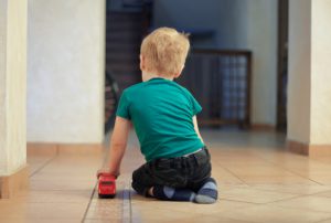 child sat on the floor playing alone with a red toy bus
