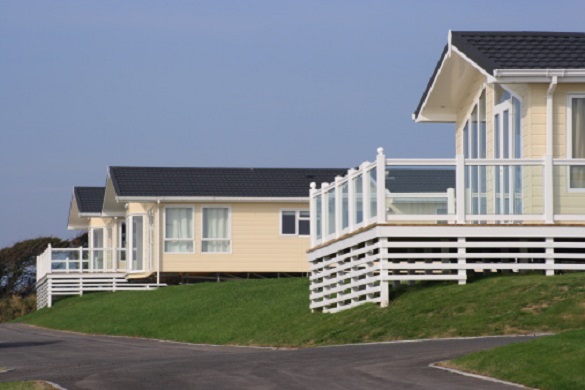 Three holiday homes perched on a grass bank with verandas and a road.