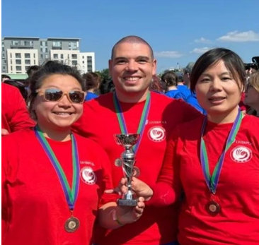 Three people with medals and red tshirts holding a trophy