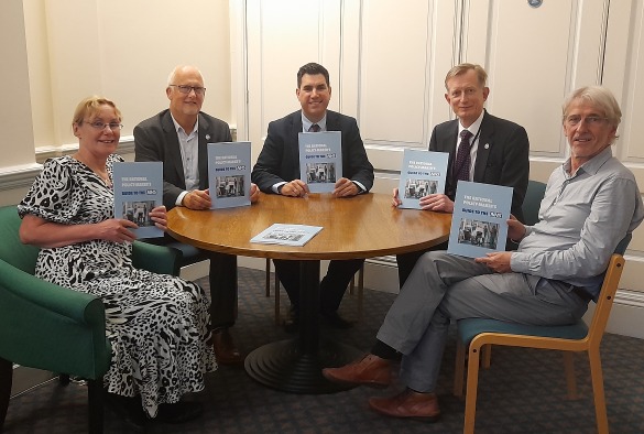 Group sit round a table holding a report entitled The Rational Policy-Maker’s Guide to the NHS