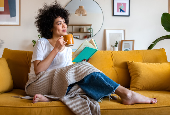A woman sitting on the couch reading and drinking coffee