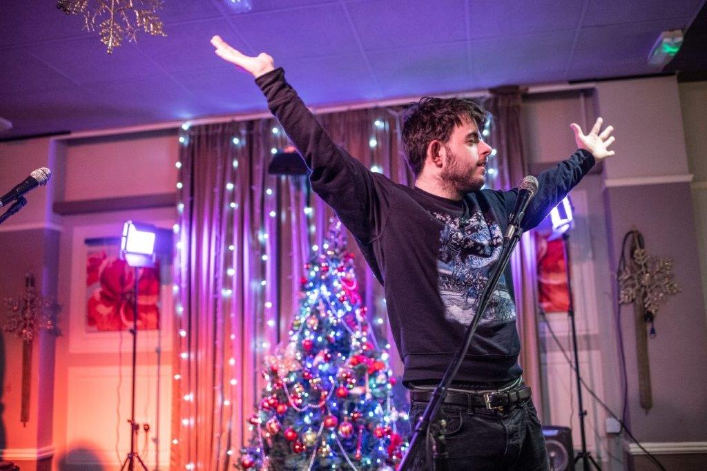 A man with his hands in the air on a stage by a christmas tree