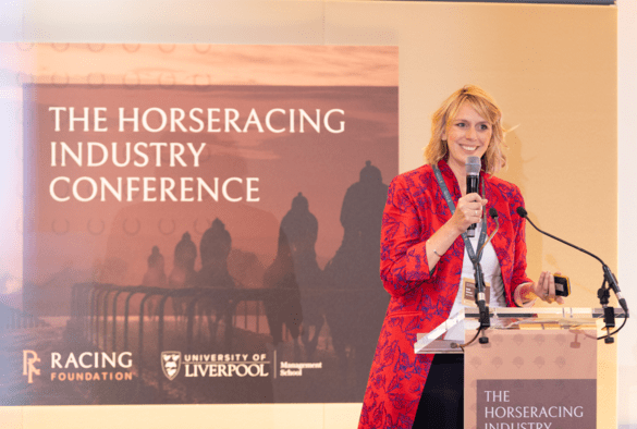 A woman speaks on a platform with horseracing industry conference written in the background