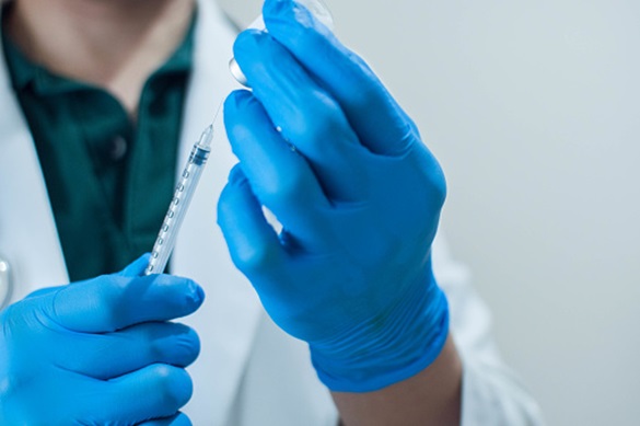 A close up photograph of a of a doctor wearing a blue protective hand gloves holding a medical syringe