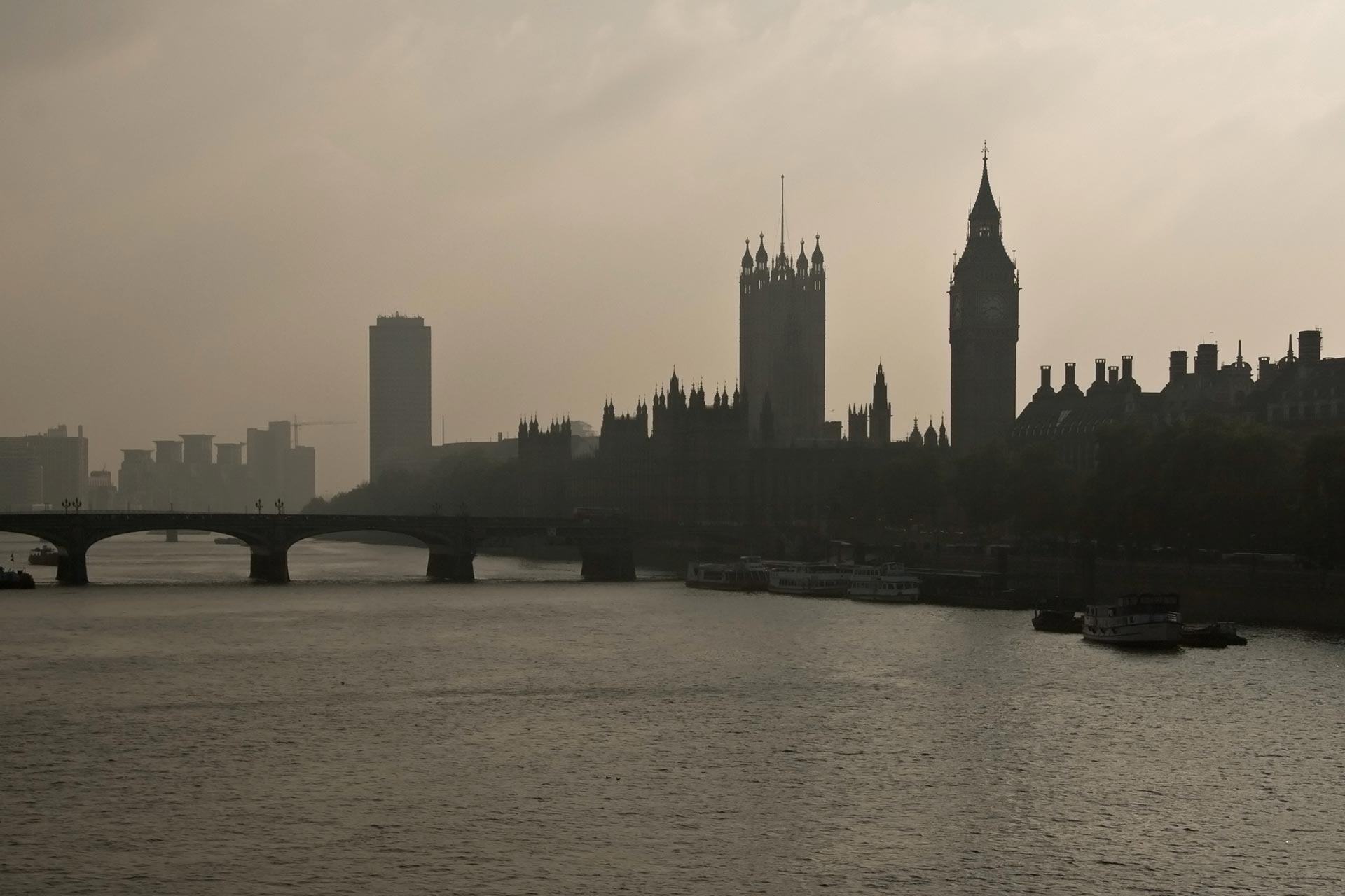 Westminster bridge over river Thames, with Big Ben silhouette in background, cloudy backlight haze.