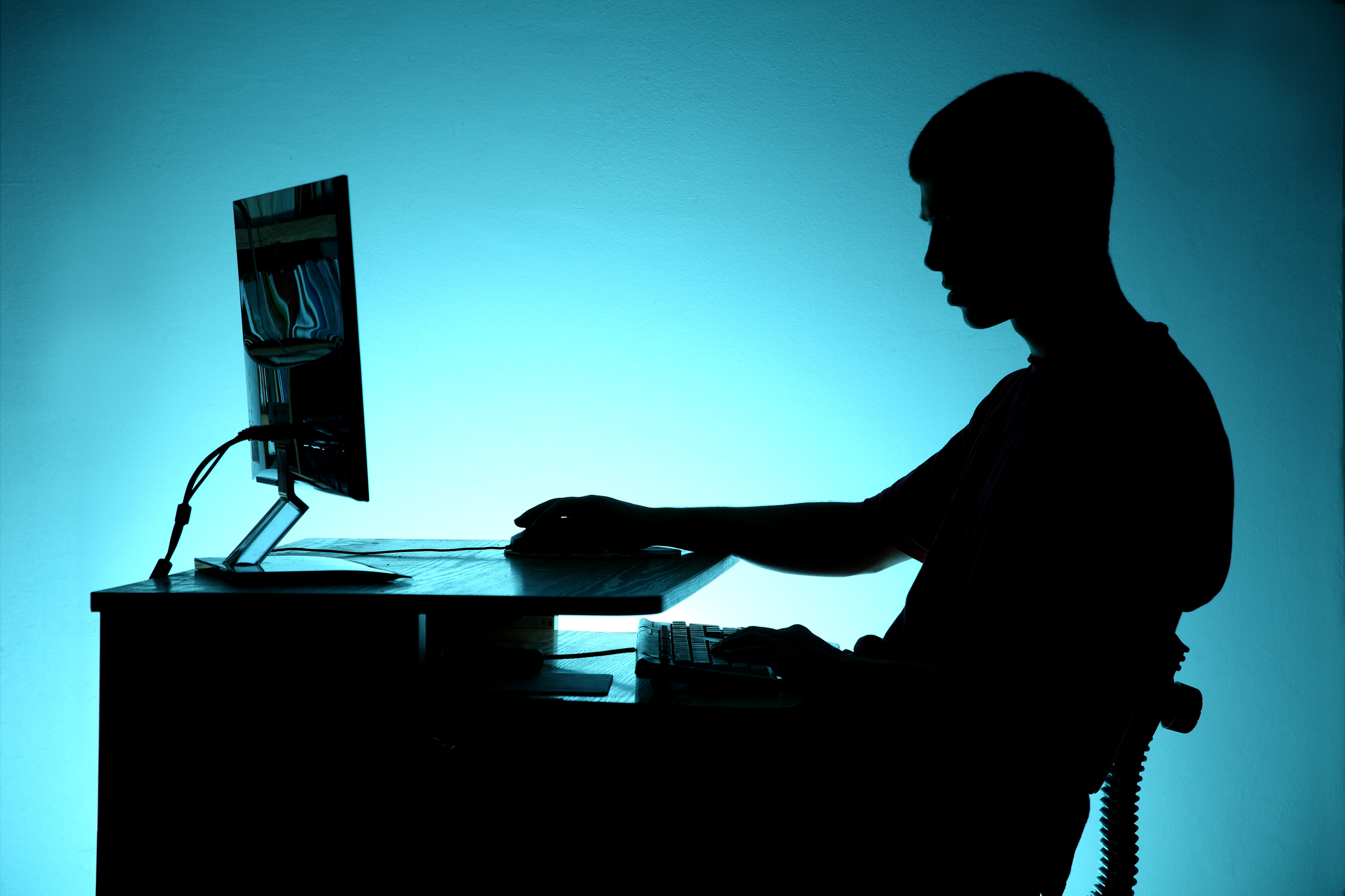 Silhouette of teenager sitting at the computer on blue background