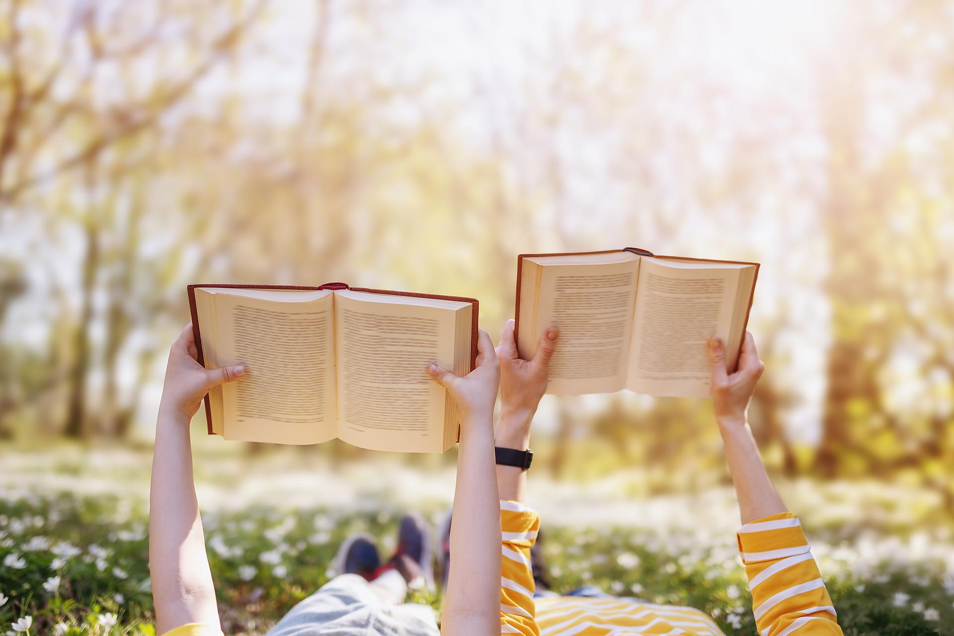 Mother and her son lying down on the beautiful spring field in the sunny park. Concept of the interesting of literature and family leisure.